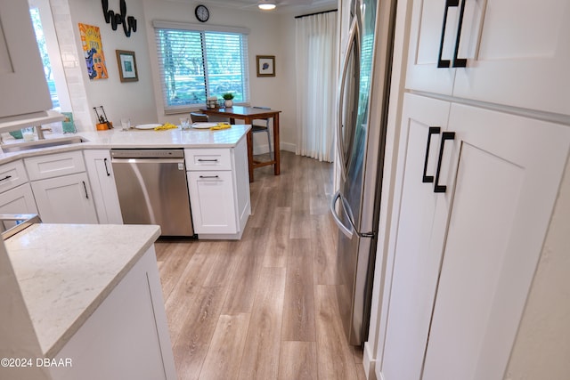 kitchen with white cabinetry, sink, stainless steel appliances, light hardwood / wood-style flooring, and a kitchen island