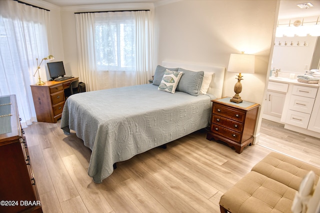 bedroom featuring connected bathroom, crown molding, and light wood-type flooring