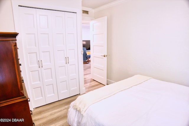 bedroom featuring light wood-type flooring, ornamental molding, and a closet