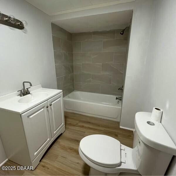 full bathroom featuring tiled shower / bath combo, toilet, vanity, and wood-type flooring