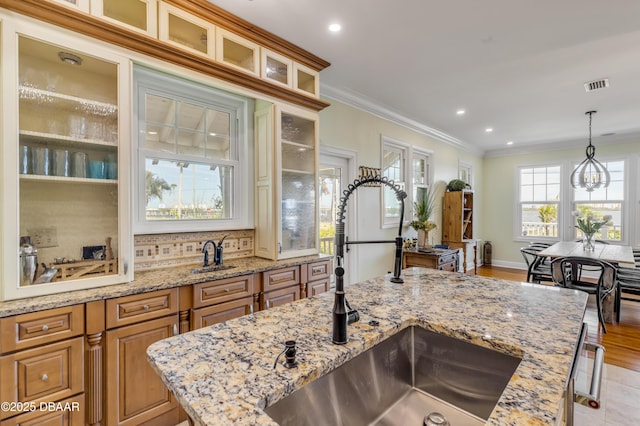 kitchen featuring decorative light fixtures, crown molding, visible vents, glass insert cabinets, and a sink