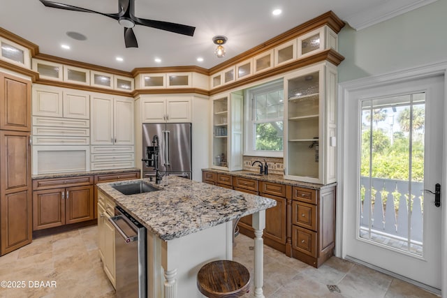 kitchen with stainless steel appliances, glass insert cabinets, a sink, an island with sink, and a kitchen bar