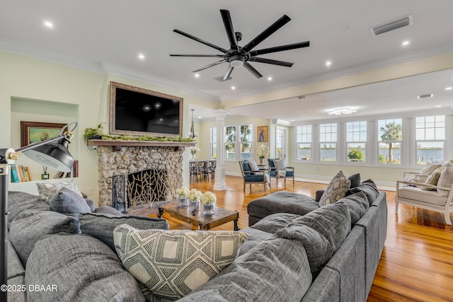 living area with decorative columns, visible vents, crown molding, light wood-type flooring, and a fireplace