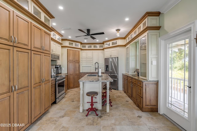 kitchen featuring light stone counters, a breakfast bar, appliances with stainless steel finishes, ornamental molding, and a kitchen island with sink