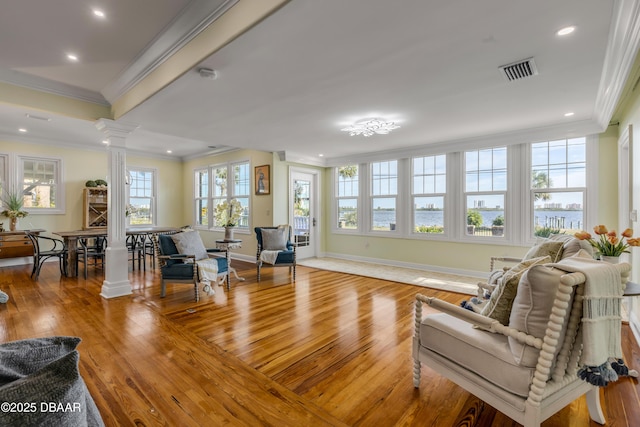 living room featuring light wood-style flooring, visible vents, baseboards, ornamental molding, and ornate columns