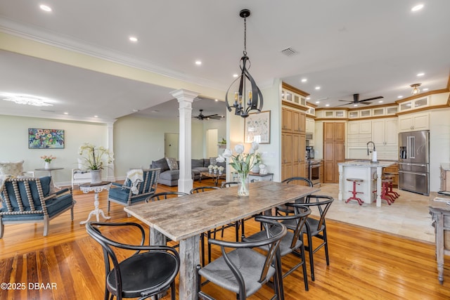 dining space featuring a ceiling fan, light wood-style floors, visible vents, and ornate columns