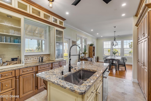 kitchen featuring a center island with sink, glass insert cabinets, crown molding, pendant lighting, and a sink