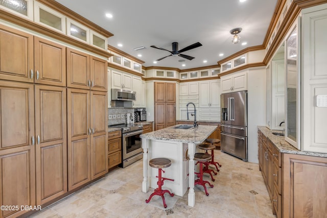 kitchen with stainless steel appliances, backsplash, a kitchen island with sink, a sink, and a kitchen bar