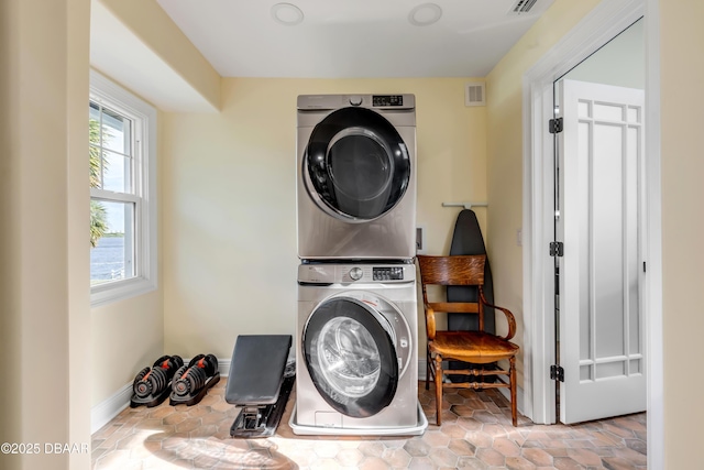 clothes washing area featuring stacked washing maching and dryer, baseboards, laundry area, and visible vents