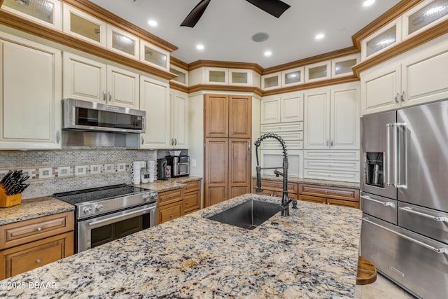 kitchen with light stone counters, appliances with stainless steel finishes, a sink, and glass insert cabinets