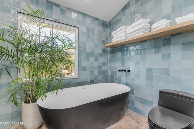 full bathroom with lofted ceiling, a freestanding tub, and tile walls