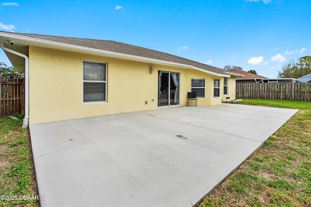 rear view of property featuring a patio, roof with shingles, fence, and stucco siding