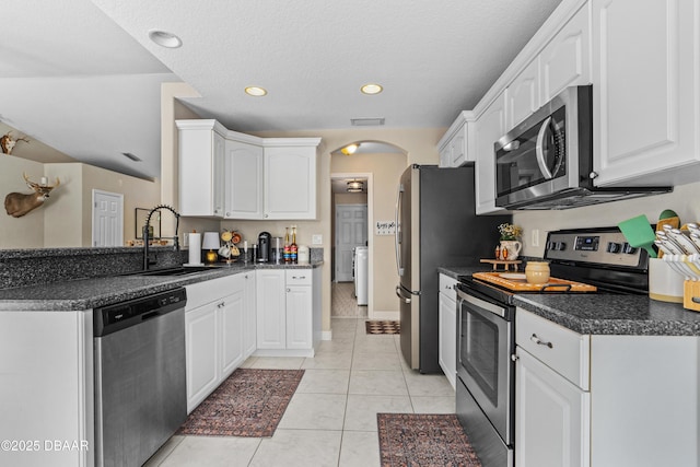 kitchen with arched walkways, dark countertops, appliances with stainless steel finishes, white cabinetry, and a sink