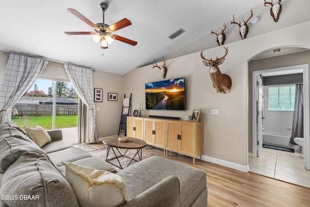 living area with arched walkways, visible vents, light wood-style floors, vaulted ceiling, and a textured ceiling