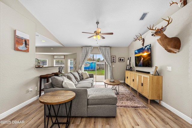 living room featuring visible vents, vaulted ceiling, baseboards, and wood finished floors