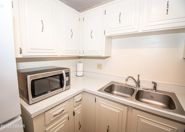 kitchen with white refrigerator, white cabinetry, sink, and a textured ceiling