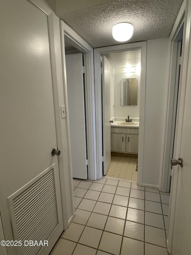 hallway featuring a textured ceiling, light tile patterned floors, and sink