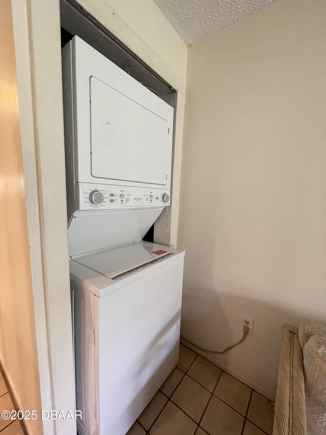 laundry room with a textured ceiling, light tile patterned floors, and stacked washer and dryer