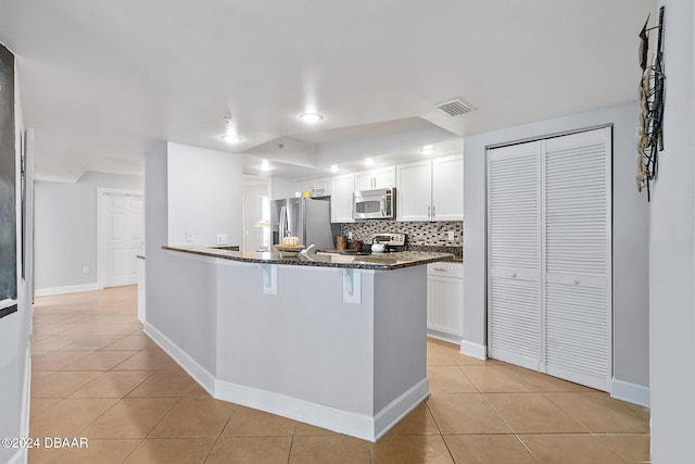 kitchen featuring light tile patterned floors, stainless steel appliances, a kitchen bar, and white cabinetry