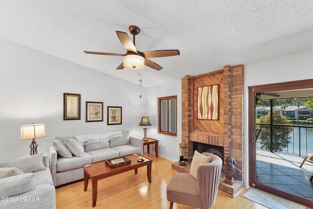 living room featuring light hardwood / wood-style floors, ceiling fan, a textured ceiling, a brick fireplace, and vaulted ceiling