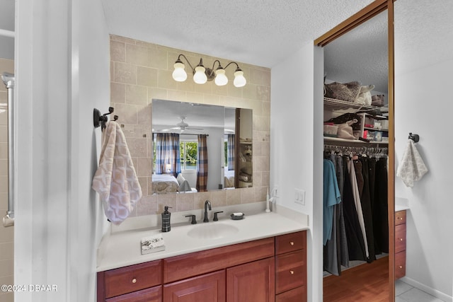 bathroom with tile walls, wood-type flooring, vanity, a textured ceiling, and ceiling fan