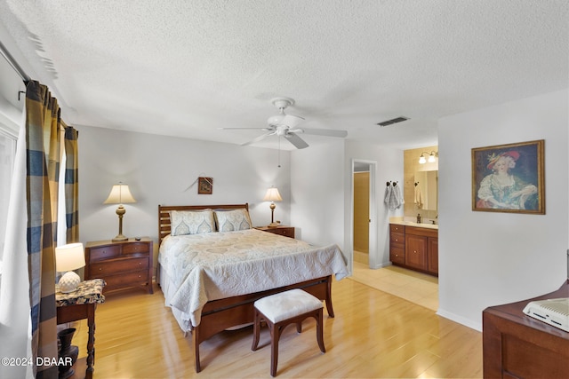 bedroom featuring light wood-type flooring, a textured ceiling, ceiling fan, and ensuite bath