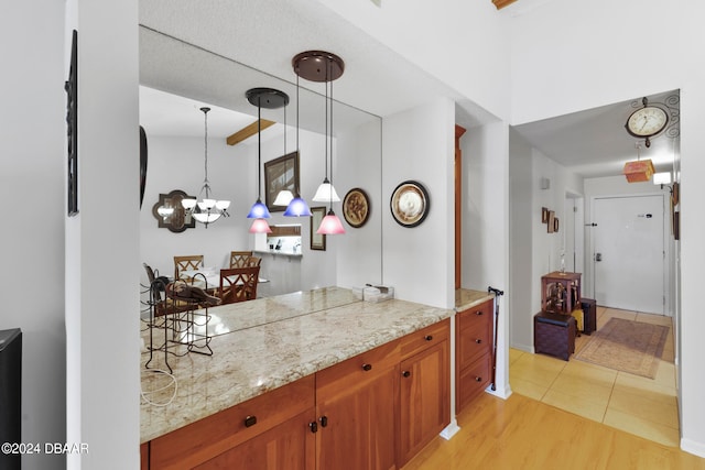 kitchen featuring light hardwood / wood-style floors, lofted ceiling, light stone counters, an inviting chandelier, and pendant lighting