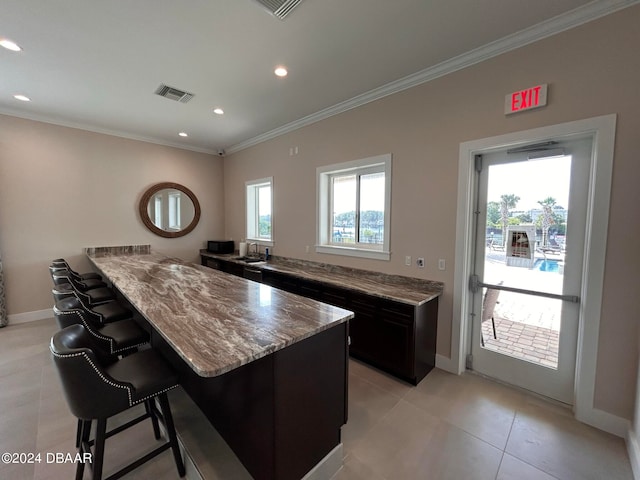 kitchen featuring light stone countertops, sink, a kitchen bar, light tile patterned floors, and ornamental molding