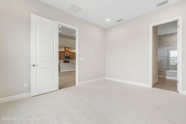 unfurnished bedroom with ensuite bath and light colored carpet