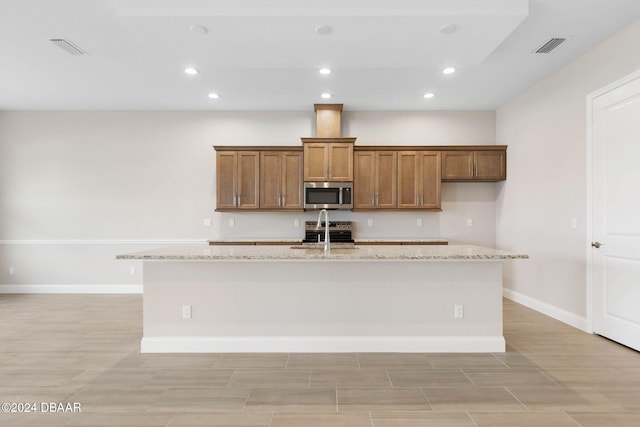 kitchen with light stone countertops, appliances with stainless steel finishes, and an island with sink