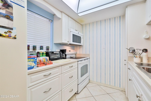 kitchen featuring white cabinets, a skylight, light tile patterned flooring, and white appliances