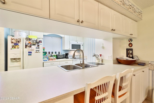 kitchen with sink, kitchen peninsula, a kitchen bar, white appliances, and white cabinets