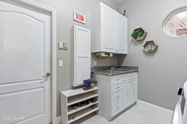 kitchen with dark countertops, light tile patterned floors, baseboards, a sink, and white cabinetry