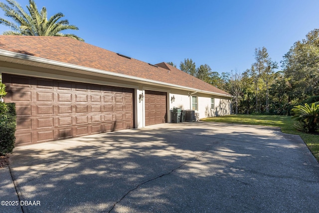 view of side of home featuring central air condition unit, driveway, a shingled roof, and a garage