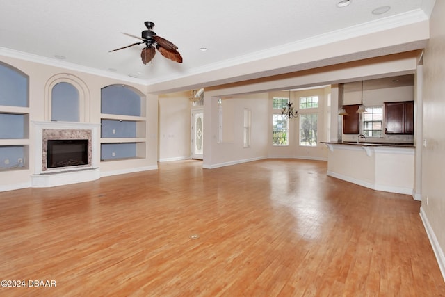 unfurnished living room with built in shelves, light wood-type flooring, crown molding, and ceiling fan with notable chandelier