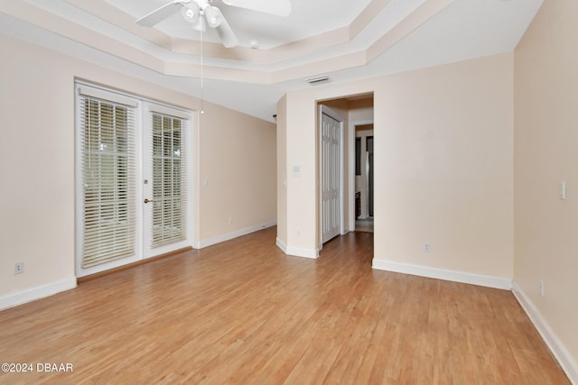 empty room featuring a tray ceiling, ceiling fan, and light wood-type flooring