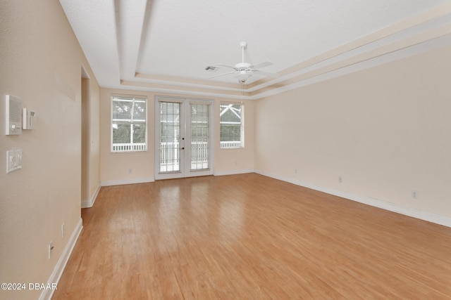 empty room featuring a raised ceiling, ceiling fan, and light wood-type flooring