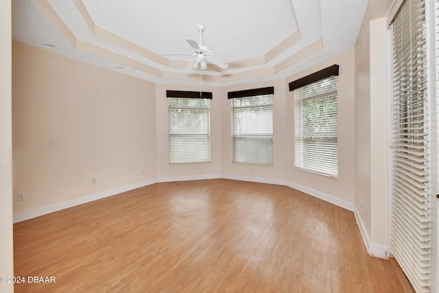 unfurnished room with ceiling fan, light hardwood / wood-style floors, and a tray ceiling