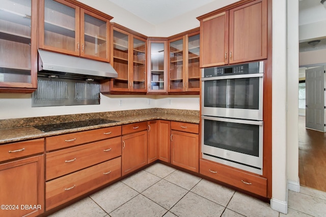 kitchen featuring black electric cooktop, double oven, dark stone counters, and light tile patterned flooring