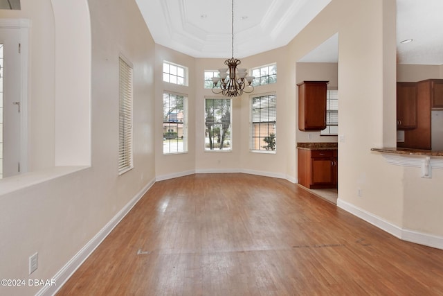 unfurnished dining area with a chandelier, light wood-type flooring, a raised ceiling, and crown molding