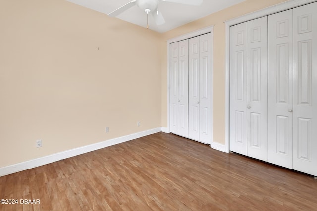 unfurnished bedroom with hardwood / wood-style floors, two closets, and ceiling fan