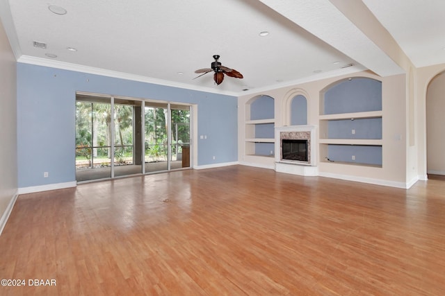 unfurnished living room featuring a high end fireplace, light wood-type flooring, ceiling fan, crown molding, and built in features