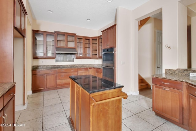 kitchen featuring dark stone counters, a textured ceiling, stainless steel double oven, light tile patterned floors, and a center island