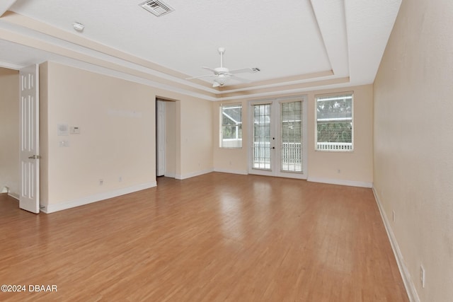 spare room featuring a tray ceiling, ceiling fan, light hardwood / wood-style flooring, and a textured ceiling