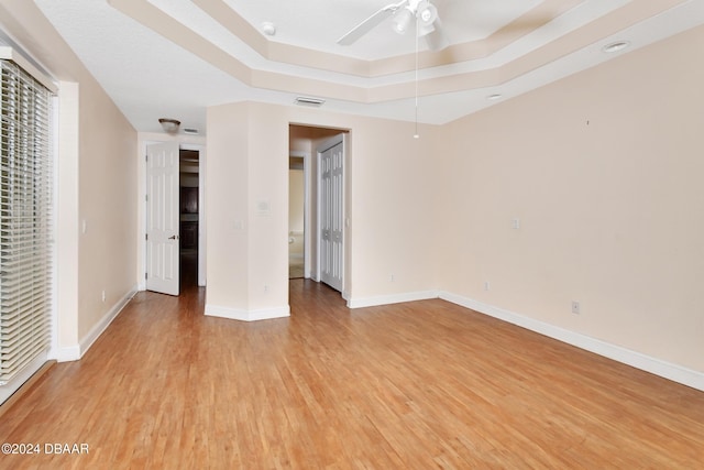 unfurnished room featuring ceiling fan, a raised ceiling, and light hardwood / wood-style flooring