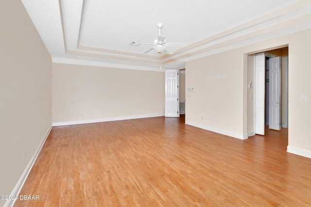 empty room with a raised ceiling, ceiling fan, and hardwood / wood-style floors