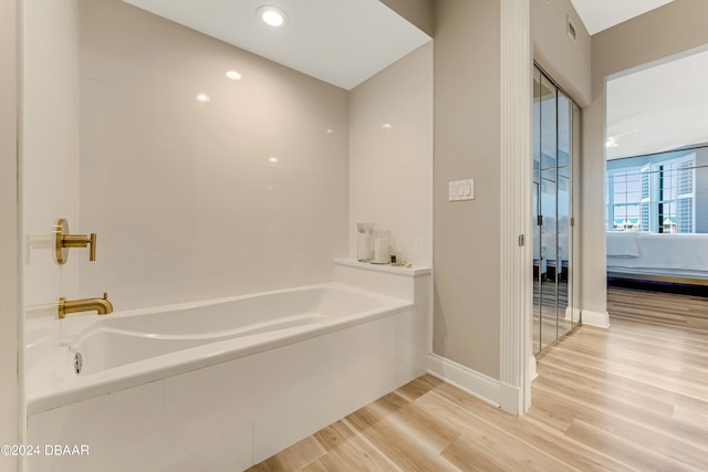 bathroom featuring a relaxing tiled tub and wood-type flooring