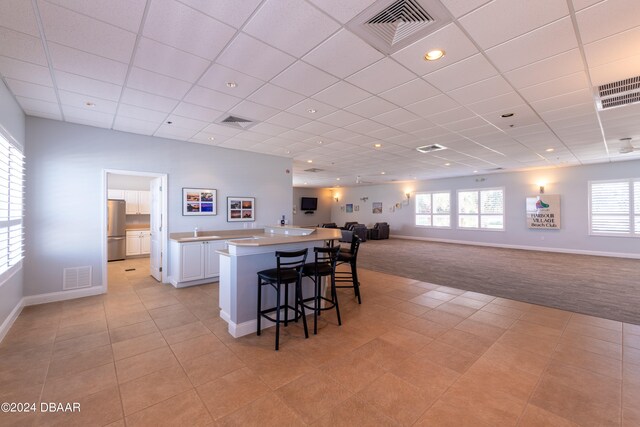 kitchen featuring stainless steel fridge, light tile patterned floors, a kitchen bar, white cabinets, and a center island