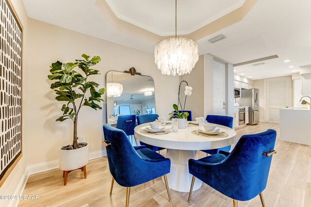 dining room with sink, a tray ceiling, a chandelier, light hardwood / wood-style flooring, and crown molding