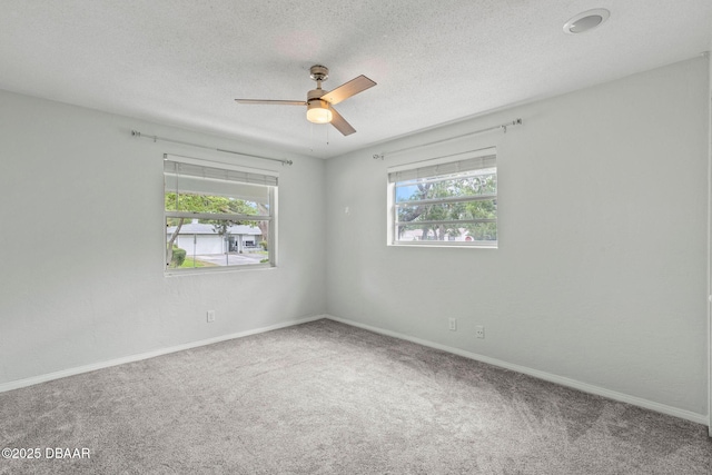 carpeted spare room with plenty of natural light, a ceiling fan, baseboards, and a textured ceiling